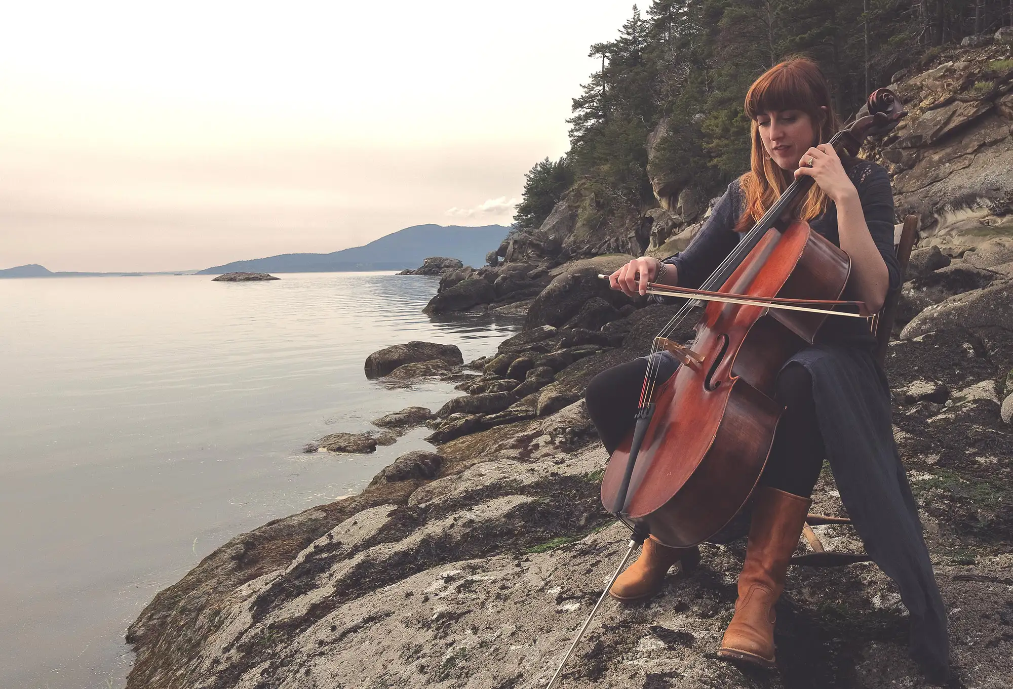 Clea playing a cello on a rocky coast